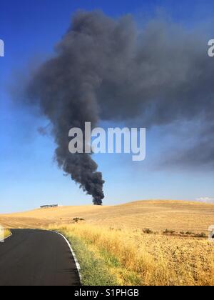 Spalte dichter schwarzer Rauch steigt von einem Brand in einem ländlichen Recyclinganlage. Stockfoto