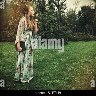 Mädchen mit Vintage-Blumenkleid, das Buch und Blumen draußen hält Stockfoto