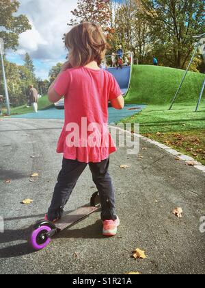 Junge Mädchen auf einem öffentlichen Spielplatz mit einem Kick scooter. Stockfoto