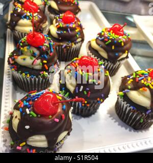 Farbenfrohe Cupcakes mit Schokoladenglasur, Streuseln und einer Kirsche Stockfoto