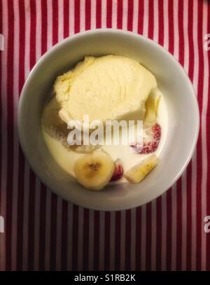 Eine Schüssel mit Obst und Eis, die in Doppelcreme schweben. Auf einem gestreiften Tischtuch sitzen. Stockfoto