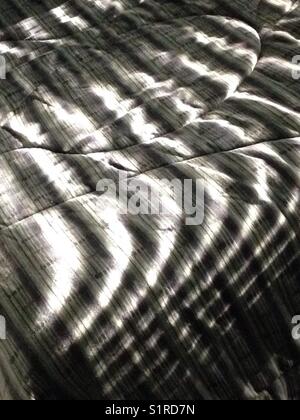 Abstrakt-stripe Schatten auf einem gestreiftem Bettüberwurf Stockfoto