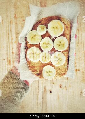 Bananenscheiben und Erdnußbutter auf Roggen Toast in papiertuch von Person über Holz- Tabelle gehalten werden Stockfoto