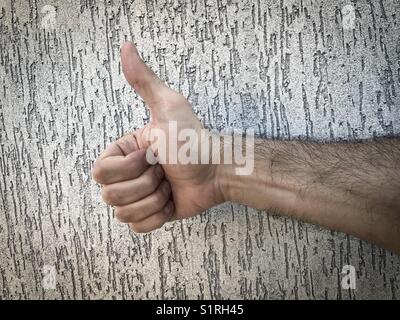 Des Menschen Hand tun einen Daumen nach oben Signal gegen eine graue Wand Stockfoto