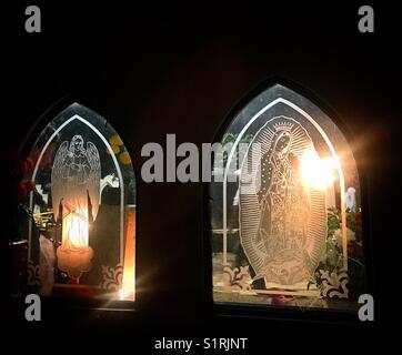 Windows mit dem Bild eines Engels und Unserer Lieben Frau von Guadalupe, die von Kerzen auf dem Friedhof leuchtet während Tag der Toten in San Gregorio Atlapulco, Xochimilco, Mexiko Stadt. Stockfoto