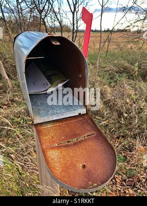 Öffnen Sie den alten, rostigen Briefkasten am Straßenrand mit der roten Flagge oben und Post drinnen Stockfoto