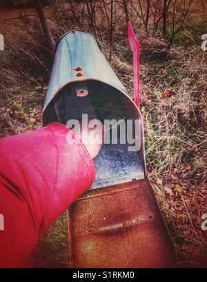 Der Arm der Person greift in die offene Mailbox, um neue Post zu erhalten Stockfoto