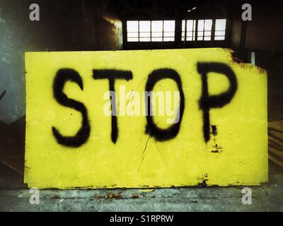 Besprühen Sie ein schwarzes Wort auf ein altes gelbes Schild am Eingang zur verlassenen Garage Stockfoto