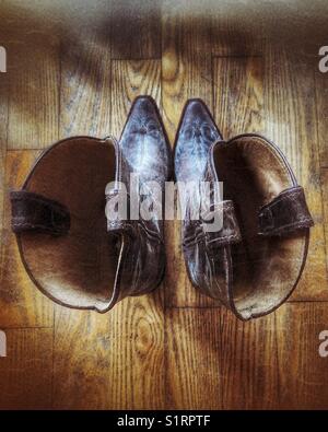 Ich schaue in ein altes Paar Cowgirl-Stiefel auf einem Holzboden herunter Stockfoto