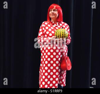 Kaukasische Frau mittleren Alters, gekleidet als japanische Künstlerin Yayoi Kusama, hält gepunkteten Kürbis für American Halloween Stockfoto