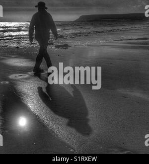 Silhouette und Schatten eines Menschen in einen Hut zu Fuß am Strand entlang. Schwarz und Weiß. Stockfoto