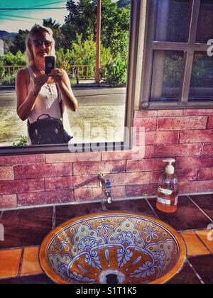 Eine Frau nimmt eine selfie in einen Spiegel an einem strassenrand Restroom in Mexiko. Stockfoto