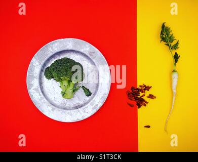 Einfache abstrakte Komposition mit Broccoli, weißer Karotte und getrockneter Chiliest auf rotem und gelbem Split-Hintergrund Stockfoto