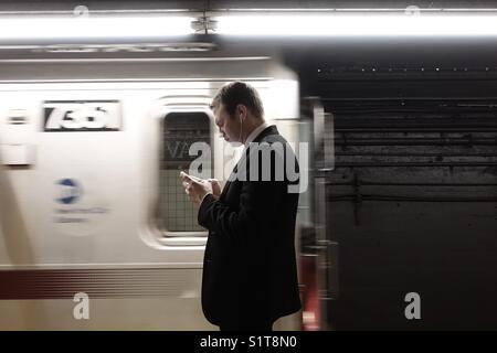 Junge Erwachsene professionelle Kontrolle in seinem Smartphone während des Wartens auf die MTA-u-bahn Stockfoto