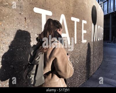 Eine junge Frau geht hinter einem Tate Modern Zeichen an der Wand außerhalb der Galerie in der Bankside in London, England am 1. Dezember 2017 Stockfoto