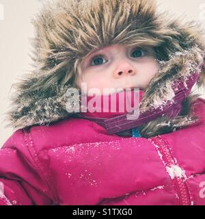 Baby Mädchen in dunkel rosa Schneeanzug und Fellimitat Trapper hat außerhalb bei starkem Schneefall in Kanada gebündelt Stockfoto