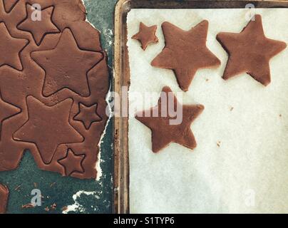 Ausschneiden sternförmige chocolate Sugar Cookies aus Teig in die Pfanne mit Pergamentpapier für Weihnachten Stockfoto