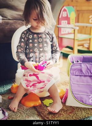 2 Jahre altes Kleinkind Mädchen sitzen auf potty Chair mit Spielzeug spielen, während wc Training Stockfoto