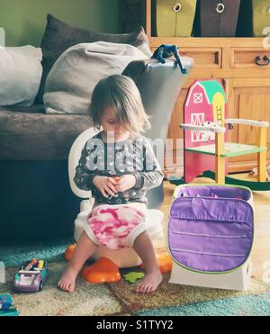 Authentische, ehrliche lifestyle Bild von Kleinkind Mädchen sitzen auf potty Chair mit Spielzeug in Familienzimmer während wc Training Stockfoto
