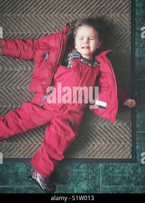 Kleinkind Mädchen in einem Wutanfall in rosa Schneeanzug auf der Fußmatte Stockfoto