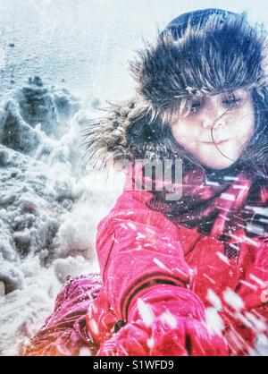 Fünf Jahre alten Mädchen in rosa Schneeanzug und braun haarige Trapper hat das Spielen in und werfen Schnee Stockfoto