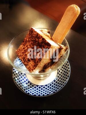 Tiramisu Dessert mit Finger Keks in einem Kegel geformte Glas Teller auf einem reich verzierten gemusterten Gericht serviert. Stockfoto