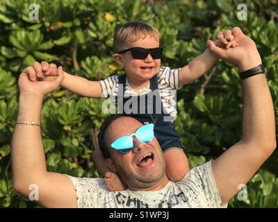 Freundliche Vater mit Sohn auf Schultern gegen Bäume Stockfoto