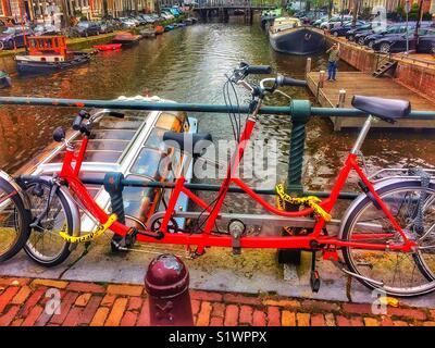 Tandem Fahrrad angekettet an Geländer oben Kanal, Amsterdam, Niederlande Stockfoto