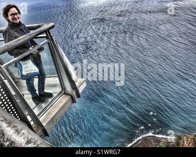 Person, die auf der Aussichtsplattform Skywalk aus Glas, 580 m über dem Meer, Miradouro do Cabo Girao, Madeira, Portugal. Stockfoto