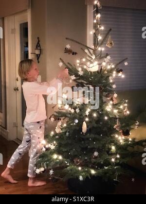 Ein Mädchen Schlafanzug tragen schmücken einen Weihnachtsbaum. Stockfoto
