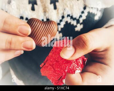 Frau essen eine herzförmige, Folie, Schokolade Herz am Valentinstag gewickelt Stockfoto