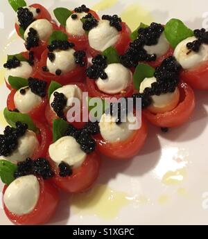 Cluster von Caprese mit Cherry Tomaten garniert mit weißen boccaccini Käse, Balsamico Essig Perlen und ein Blatt Basilikum, übergossen in extra nativem Olivenöl. Stockfoto