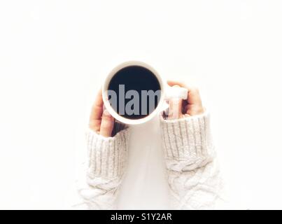 Auf der Suche nach unten von oben auf einen weißen Hintergrund mit einem Mädchen, dass eine Tasse schwarzen Kaffee und einem warmen arran Pullover tragen Stockfoto