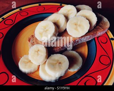 Nahaufnahme von Erdnussbutter und Bananenscheiben auf einem Stück von Roggen Toast auf eine bunte Platte Stockfoto