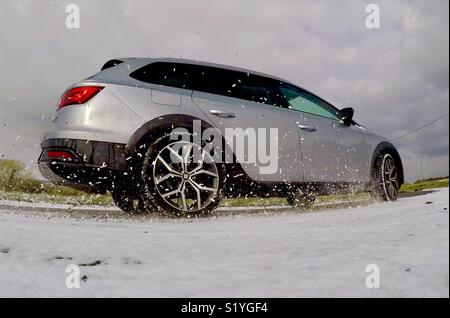 Auto sprühen Schnee als Er fährt durch eine Ecke im Winter Stockfoto