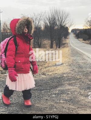 Junge schulpflichtige Mädchen zu Fuß zum Straßenrand für School Bus am Morgen zu warten Stockfoto