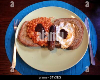 Ein vegetarisches Frühstück mit Toast, Rührei, Bohnen und eine vegetarische Wurst und braune Soße. Es sieht aus wie ein Gesicht! Stockfoto