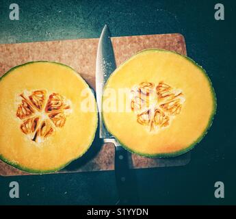 Zwei frisch geschnittenen Melone Hälften auf einem Schneidebrett mit großen Edelstahl Messer Stockfoto