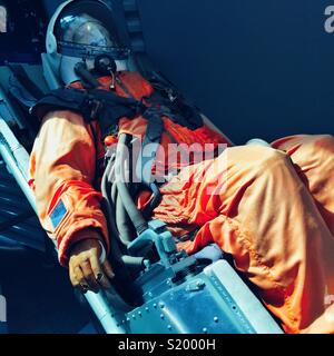 Modell der Person in orange Raumanzug zu einer Landung Stuhl im Museum gegurtet Stockfoto