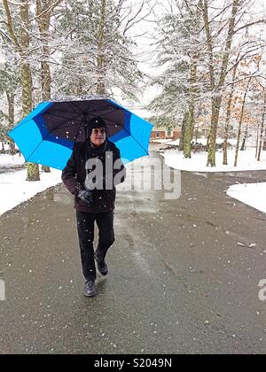 Reifer Mann mit Schirm wandern in Neu England Schneesturm, USA Stockfoto