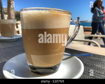 Cafe con Leche, milchig weißen Kaffee, auf einem Tisch in einem Café an der Uferpromenade im Hafen von Javea/Xabia an der Costa Blanca, Provinz Alicante, Comunidad Valenciana, Spanien Stockfoto