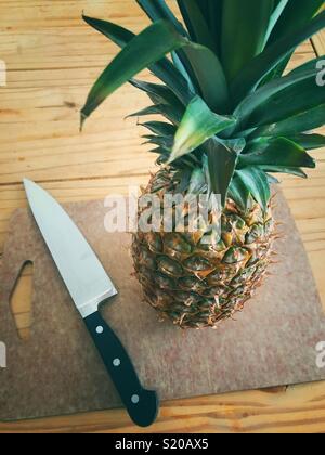 Ganze Ananas und großes Messer auf Schneidebrett auf rustikalen Holztisch Stockfoto