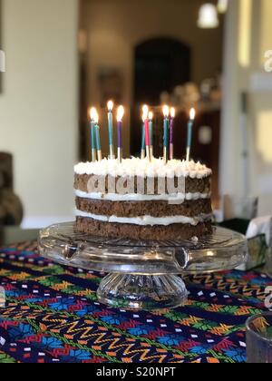 Bunte Karottenkuchen Geburtstag Kuchen mit zehn Kerzen angezündet und festlichen Tischdecke auf Crystal platter Stockfoto