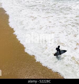 Eine männliche Surfer geht hinaus in die Brandung. Manhattan Beach, Kalifornien, USA. Stockfoto