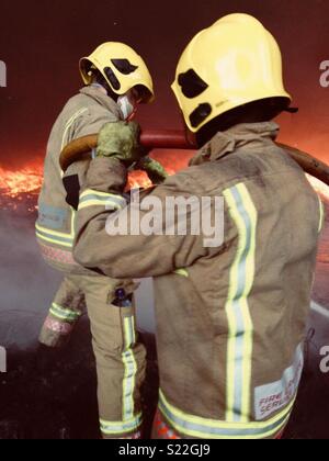 Zwei Feuerwehrmänner arbeiten zusammen, um ein Feuer zu setzen Stockfoto