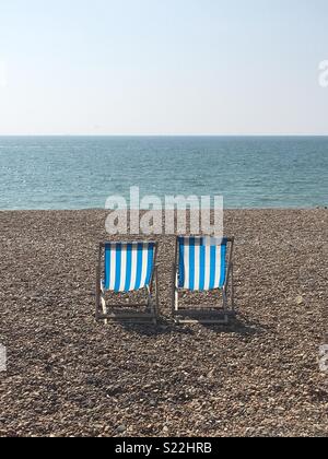 Zwei blau-weiß gestreifte Liegestühle am Brighton Beach, Großbritannien - eine typische englische Seeszene.