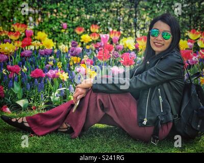 Eine Dame sitzt auf dem Boden und posiert für ein Foto vor einem blumenbeet der Tulpen. Stockfoto