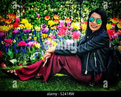 Eine Dame sitzt auf dem Boden und posiert für ein Foto vor einem blumenbeet der Tulpen. Stockfoto