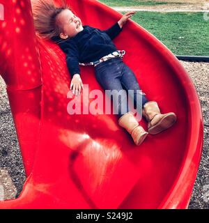 Kleinkind Mädchen glücklich lächelnd, während Sie einen roten Rutschbahn Stockfoto