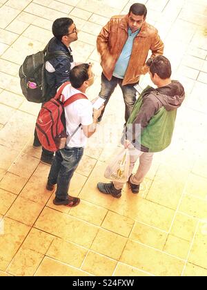 Vier Männer warten auf Ihren Zug und Ihr Smartphone prüfen Stockfoto